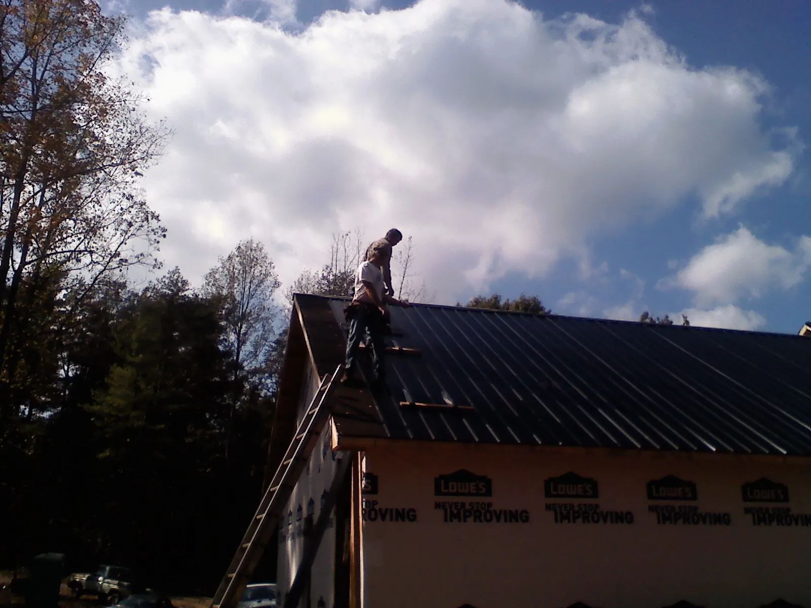 Roofer fastening dark metal panels high against a cloudy sky, from a Roof Inspection job in Berkley