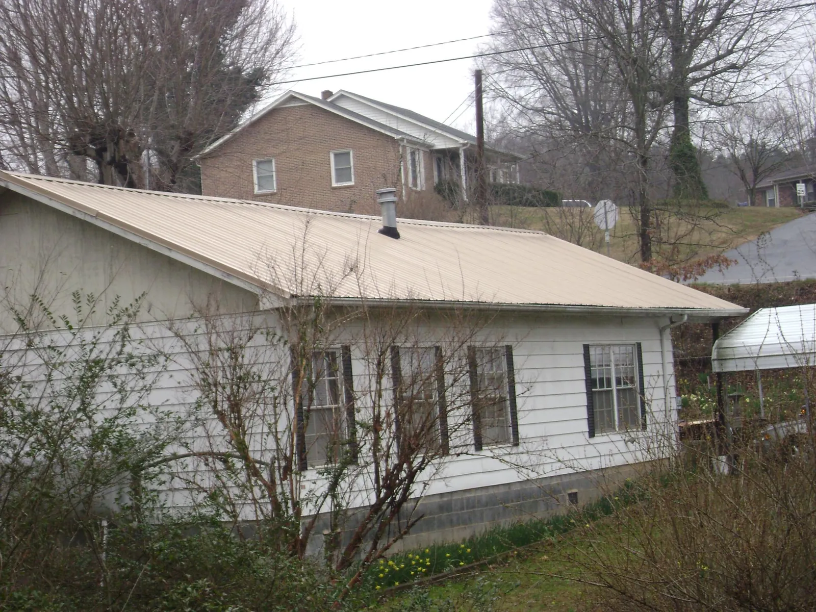 Tan metal roof on a white sided house set into a hillside — Commercial Roofing by Roofing Brothers in Berkley